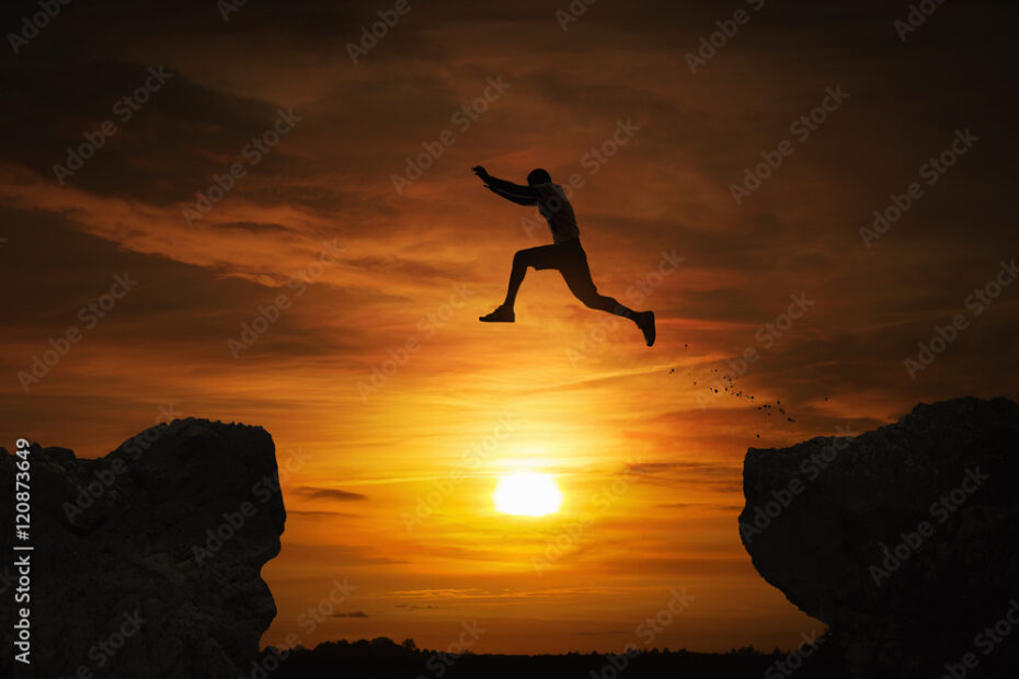 Silhouette of a man jumping over abyss at sunset with copy space